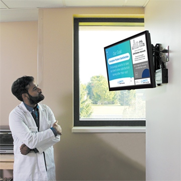 A young doctor looks up at a screen in the break room of the medical practice where he works and sees information about COVIDSitters, a program providing free services to COVID-19 frontline healthcare workers.