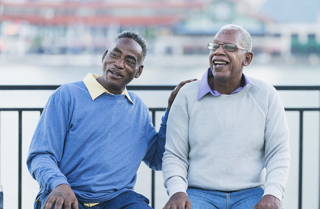 Two senior African American men sitting on a bench near a riverfront.