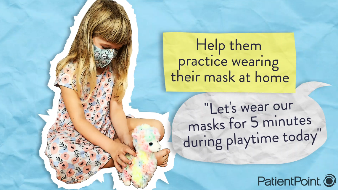A little girl sits crossed-legged wearing a face mask and playing with a stuffed amimal.