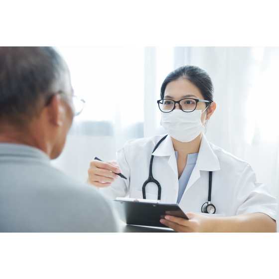 Woman doctor with face mask holding tablet sitting across table from male patient talking