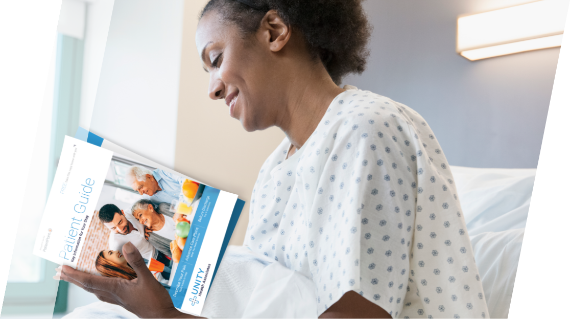 Woman wearing a hospital gown reading a patient guide while sitting in a hospital bed.