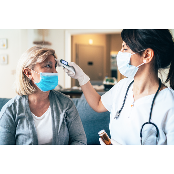Young woman nurse and middle age female patient sitting in waiting room wearing face masks while nurse checks the temperature of patient