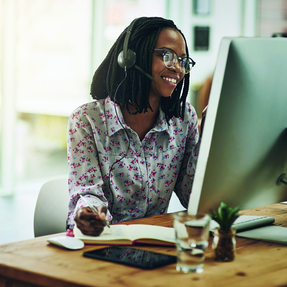 Young African American woman with headset on sitting at desk looking at computer screen smiling